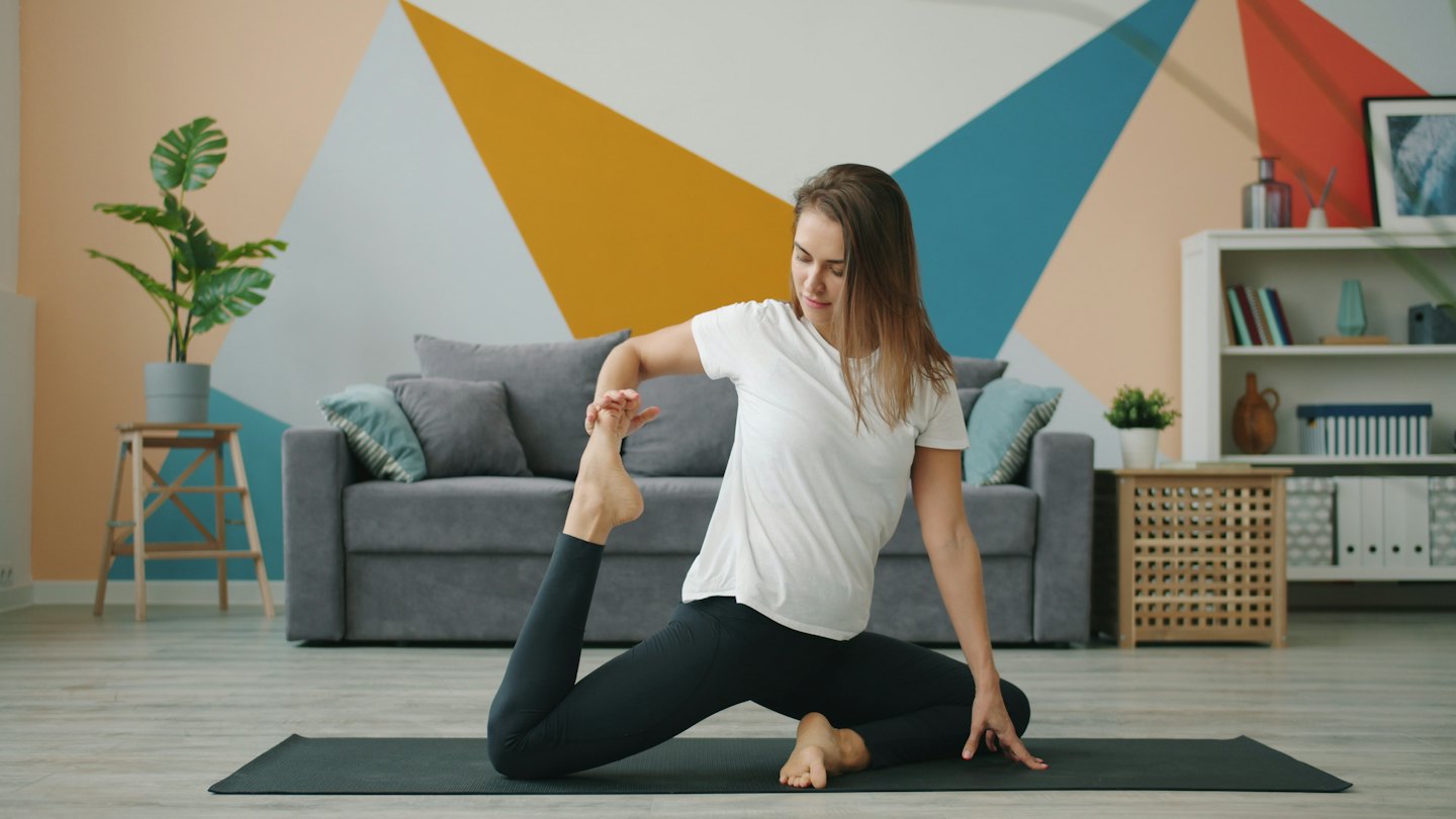 Woman in leggings performs a quad stretch on a yoga mat.