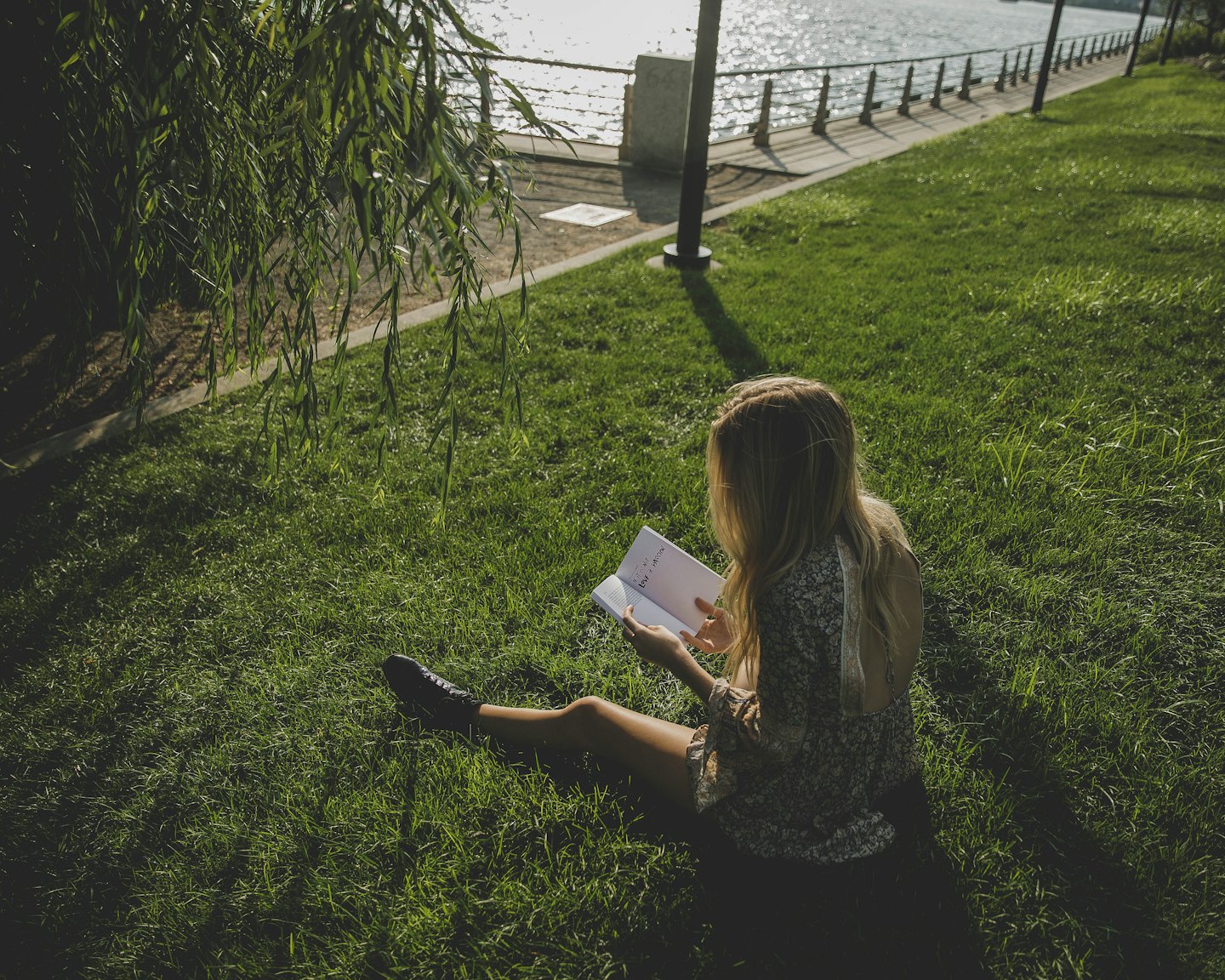 Woman reading a book on grass by a lake.