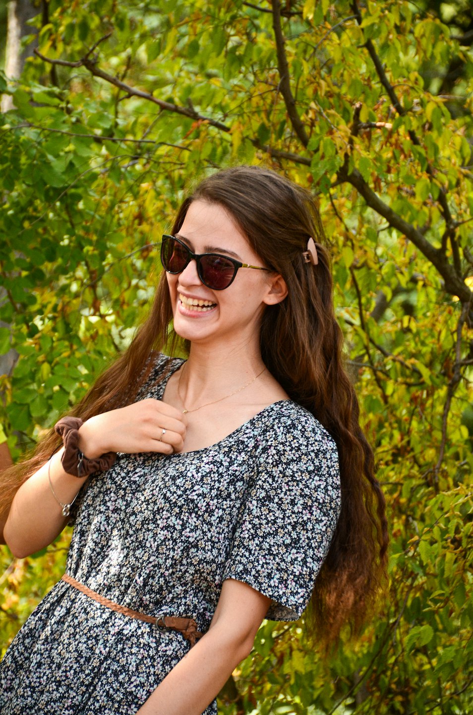 Woman in floral dress laughing outdoors near garden foliage.