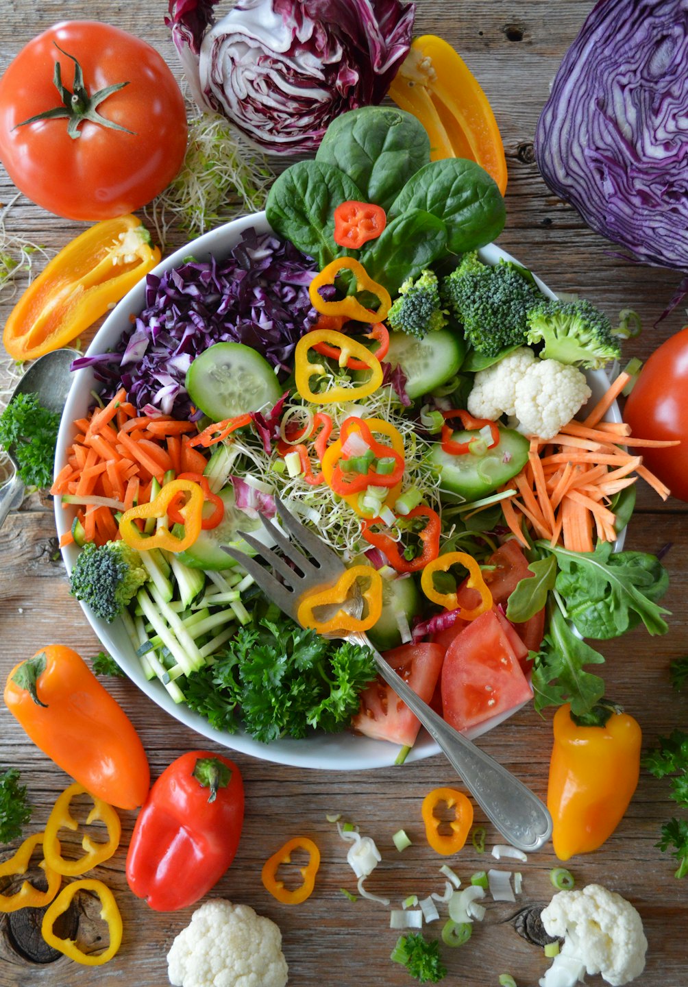 Fresh salad in a white bowl with a fork on a wooden table.