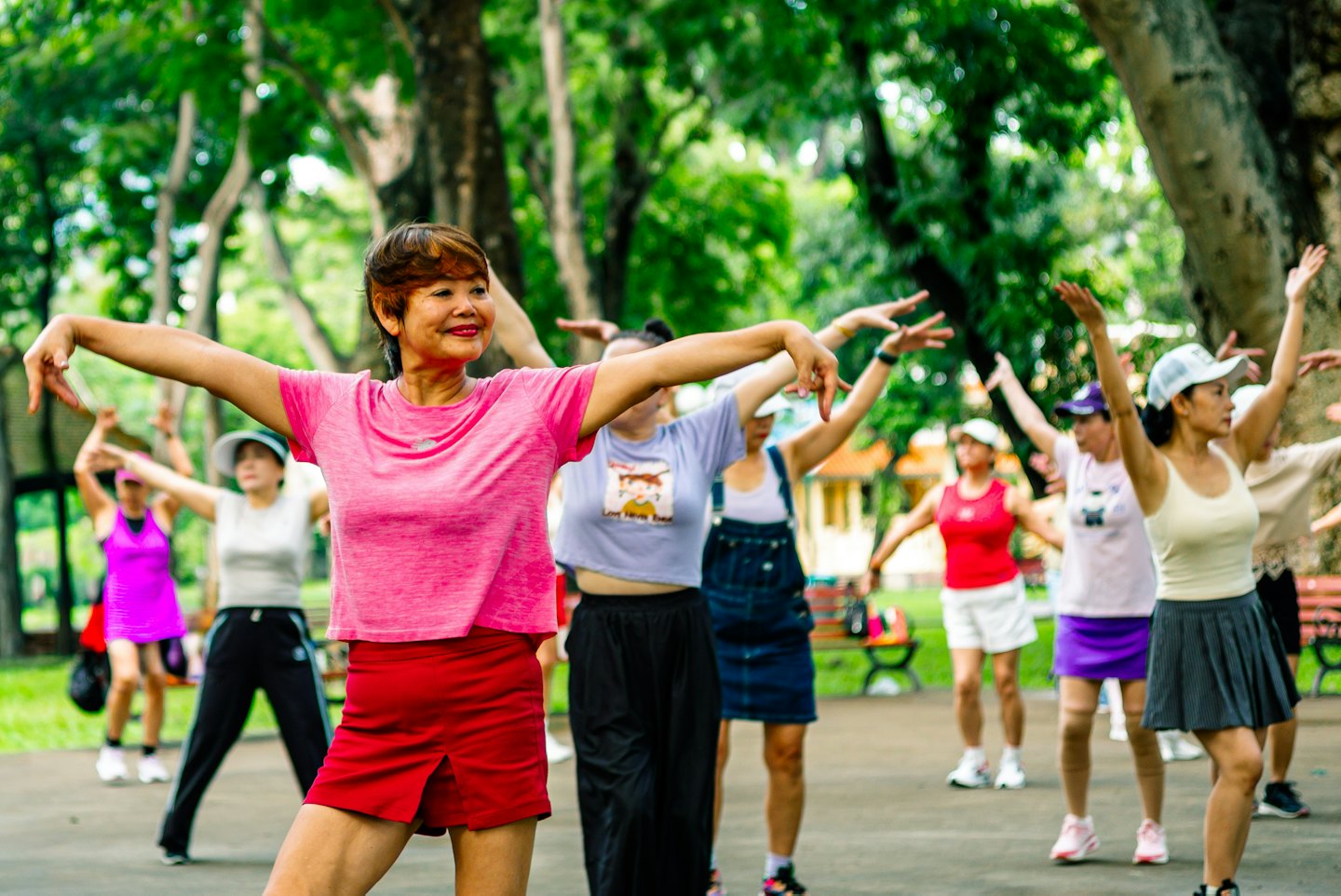 Women perform synchronized exercises together in a green park.