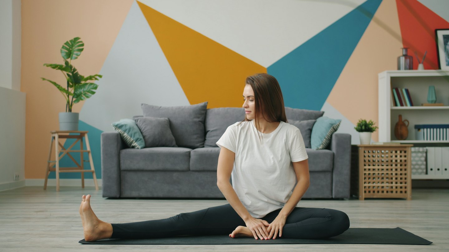 Woman stretches on a yoga mat in a modern living room.