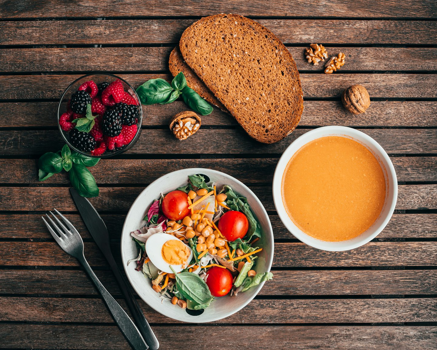 Healthy salad, soup, bread, and berries laid out on a wooden table.